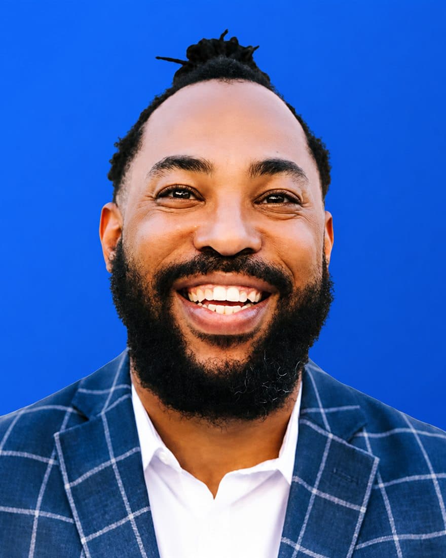 Portrait of Seneca Scott, operations lead at Aculeus, in a windowpane blazer against a signal-blue background